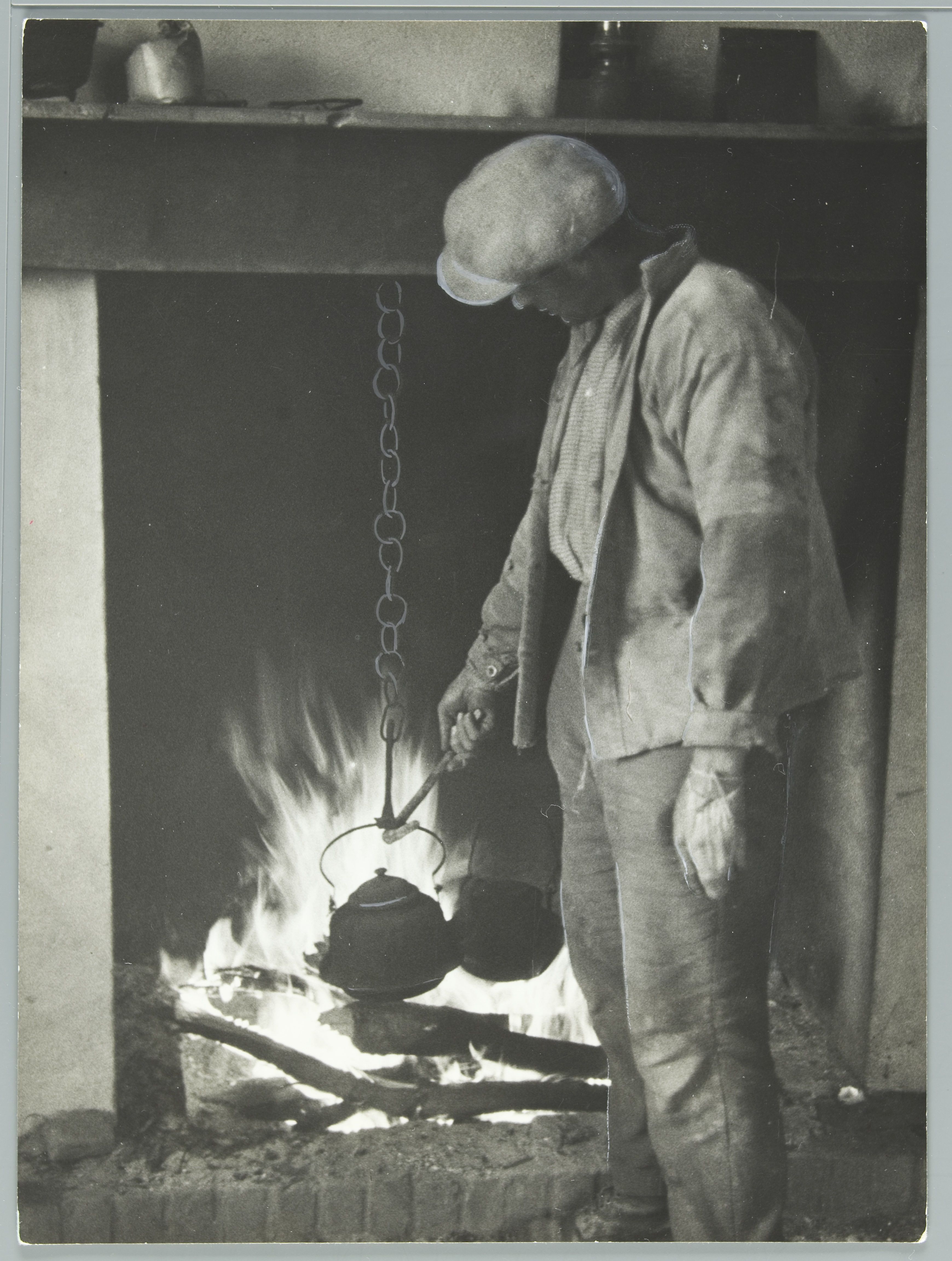 Omschrijving: (Land)arbeider houdt een ketel in het vuur: bezig met water koken om koffie te zetten in een hut in de Biesbosch. Nederland [1936].